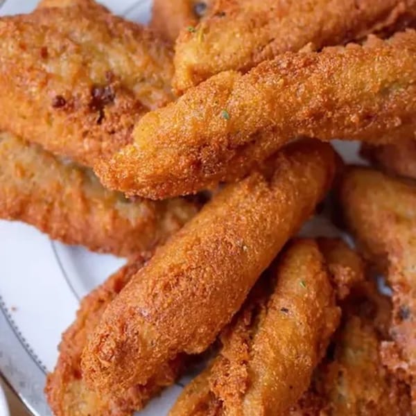Close-up of golden-brown, crispy Haitian fried plantains, some with visible seasoning, on a white plate.