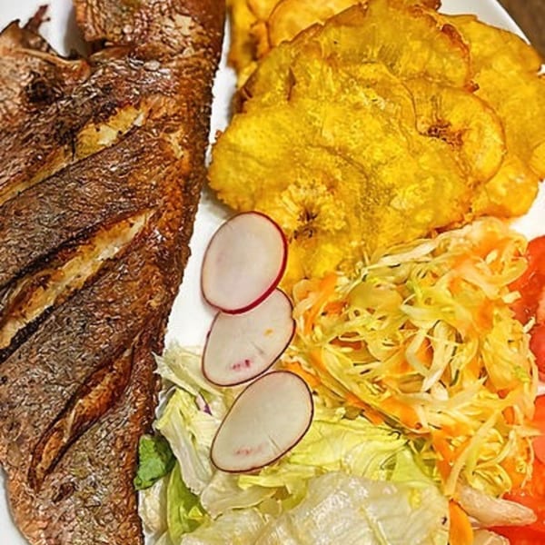 Haitian fried fish with plantains, a fresh salad, and sliced radishes on a white plate.