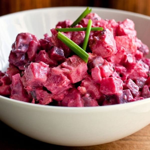A white bowl filled with vibrant red Haitian beet salad, garnished with fresh green chives.