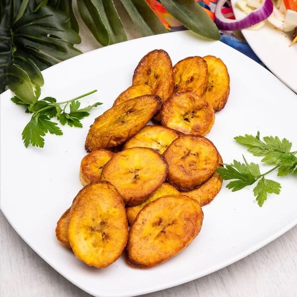 A white plate filled with golden-brown fried plantains, garnished with fresh parsley.