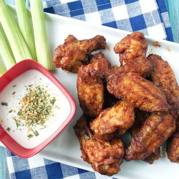 Haitian-style chicken wings with dipping sauce and celery sticks on a white platter.