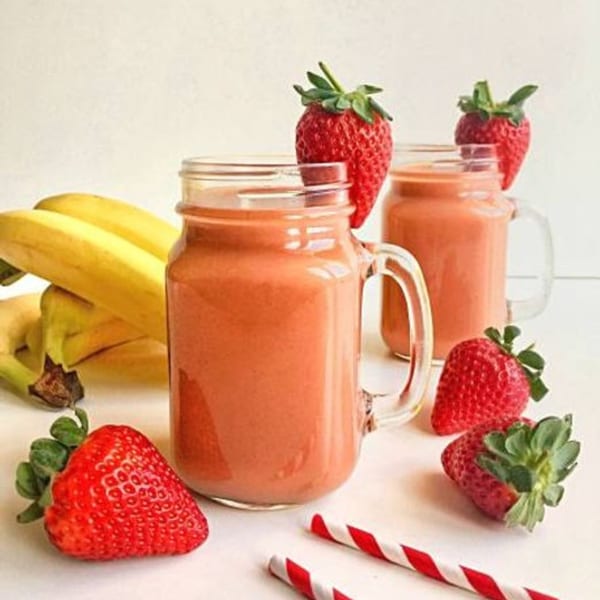 Two strawberry banana smoothies in mason jars, surrounded by fresh strawberries and bananas.