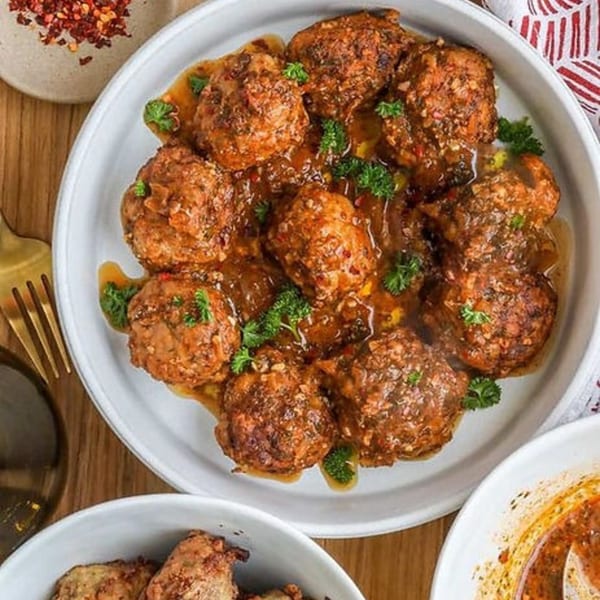 A white plate filled with Haitian meatballs in a rich sauce, garnished with fresh parsley.